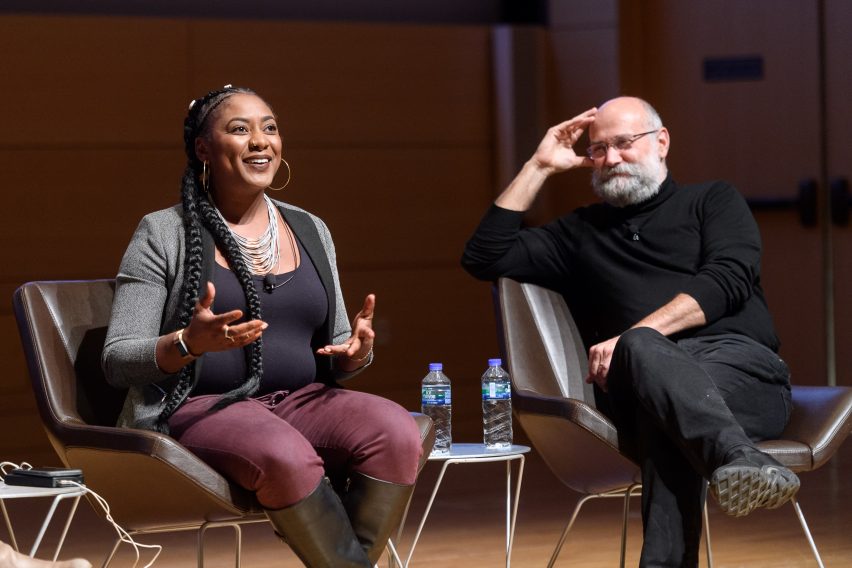 Two panelists on stage, one person is talking while the other is listening and smiling.